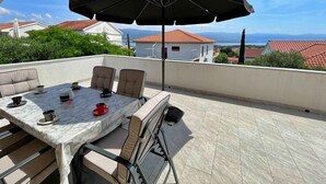 Una terraza con una mesa y sillas, un paraguas grande y vistas a casas y montañas.