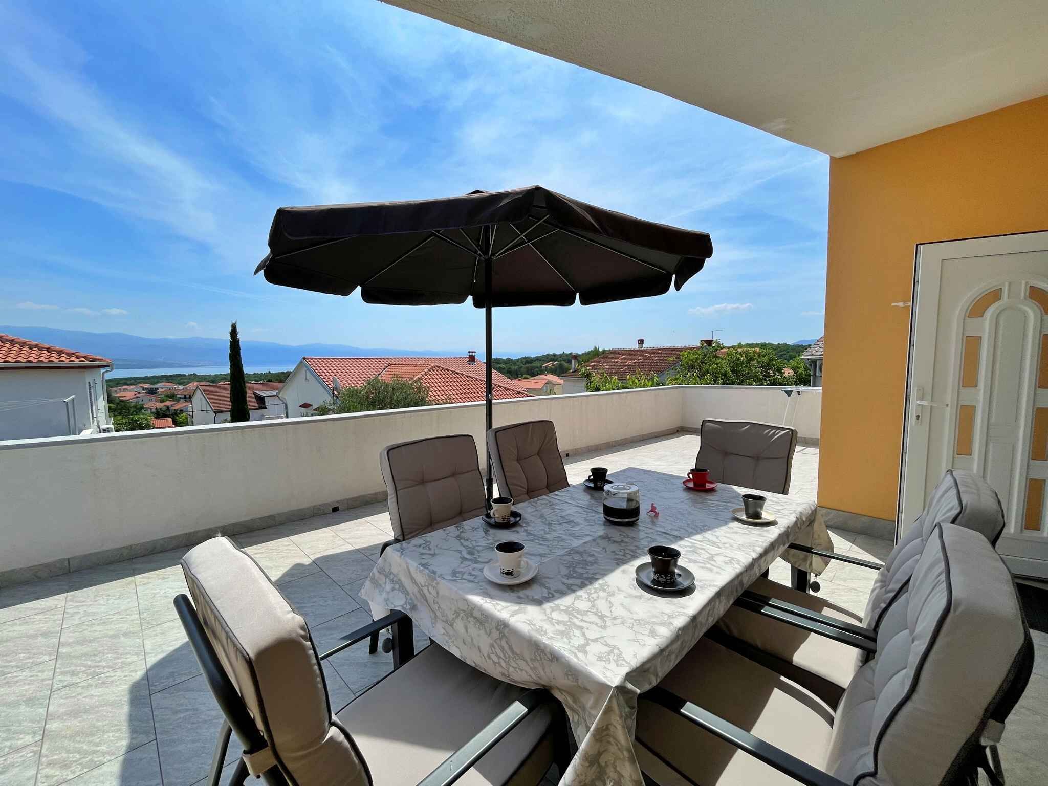 Una terraza con una mesa, sillas, una sombrilla y vistas al mar y edificios.