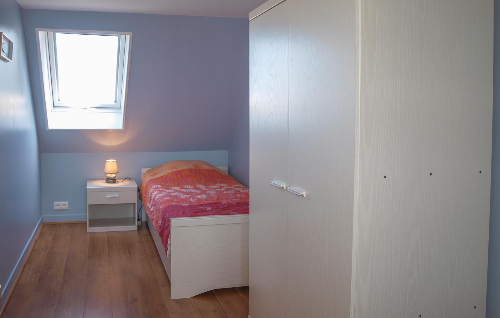 A bedroom with a single bed, a bedside table with a lamp, a window, and a wardrobe.