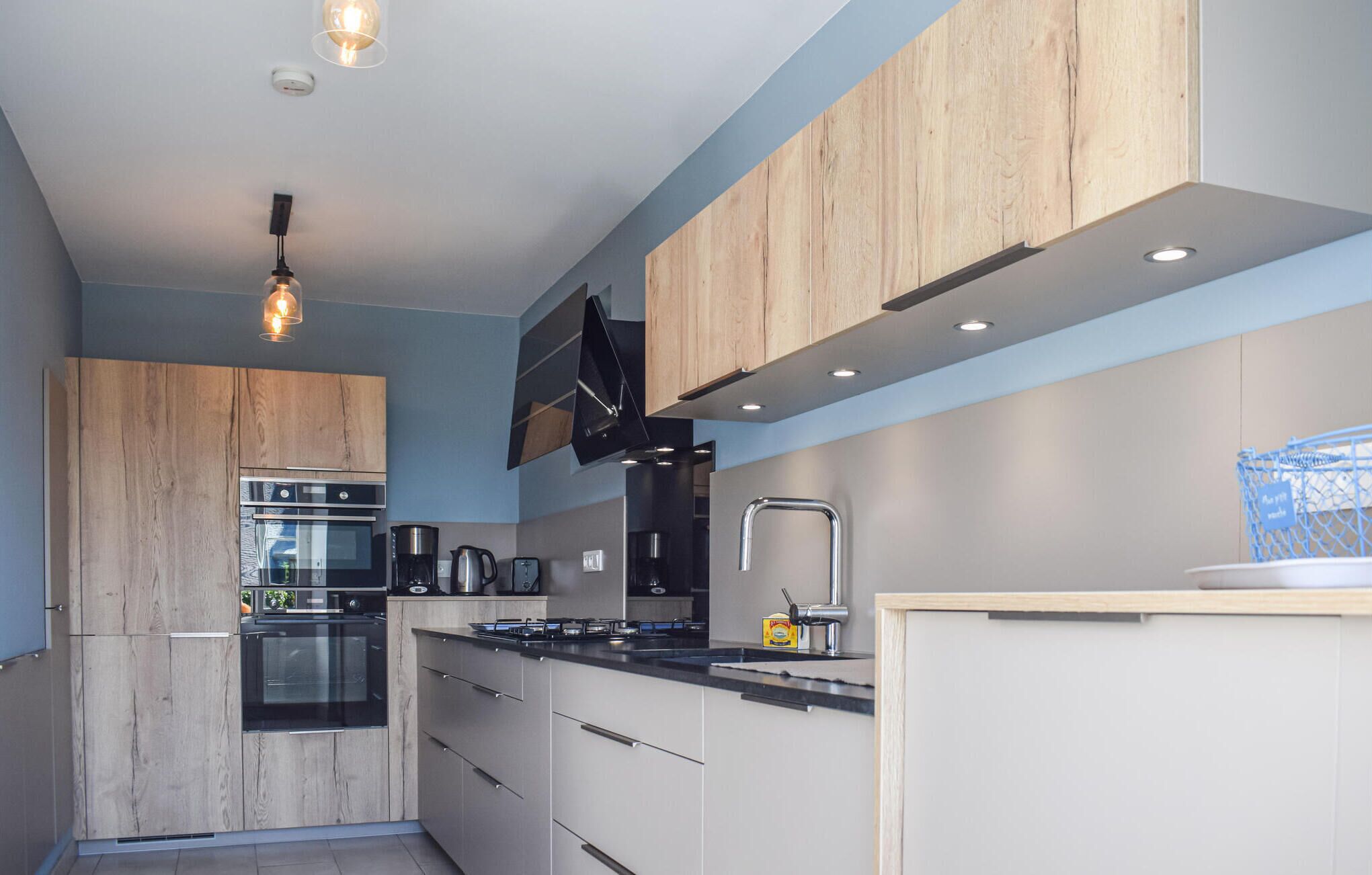 Een moderne keuken met houten kastjes, roestvrijstalen apparatuur en een zwart aanrecht.