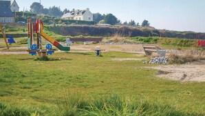 Ein Spielplatz mit Rutsche und Schaukeln, umgeben von Rasen und einigen Bänken.