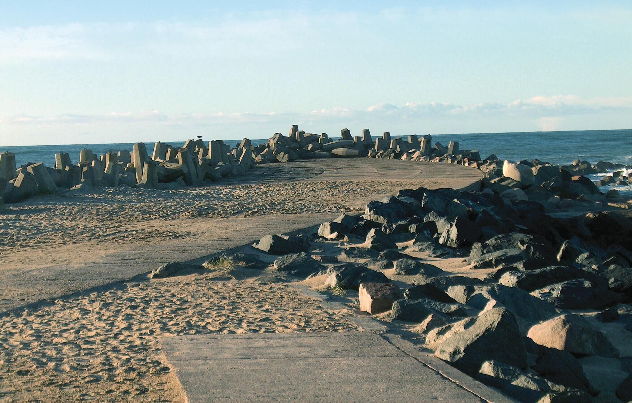 Une plage dotée d’une digue en béton et d’un sentier sablonneux menant à la mer.