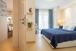 A hotel room with a bed, a bathroom with a mirror, and a shelf with a vase of flowers. - Kein Hüsung (Whg. 1) - Strandresidenz-Kühlungsborn ***** (Kühlungsborn)