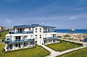 Ein mehrstöckiges Hotel mit Balkonen, Blick auf den Strand und einem Segelboot in der Ferne.