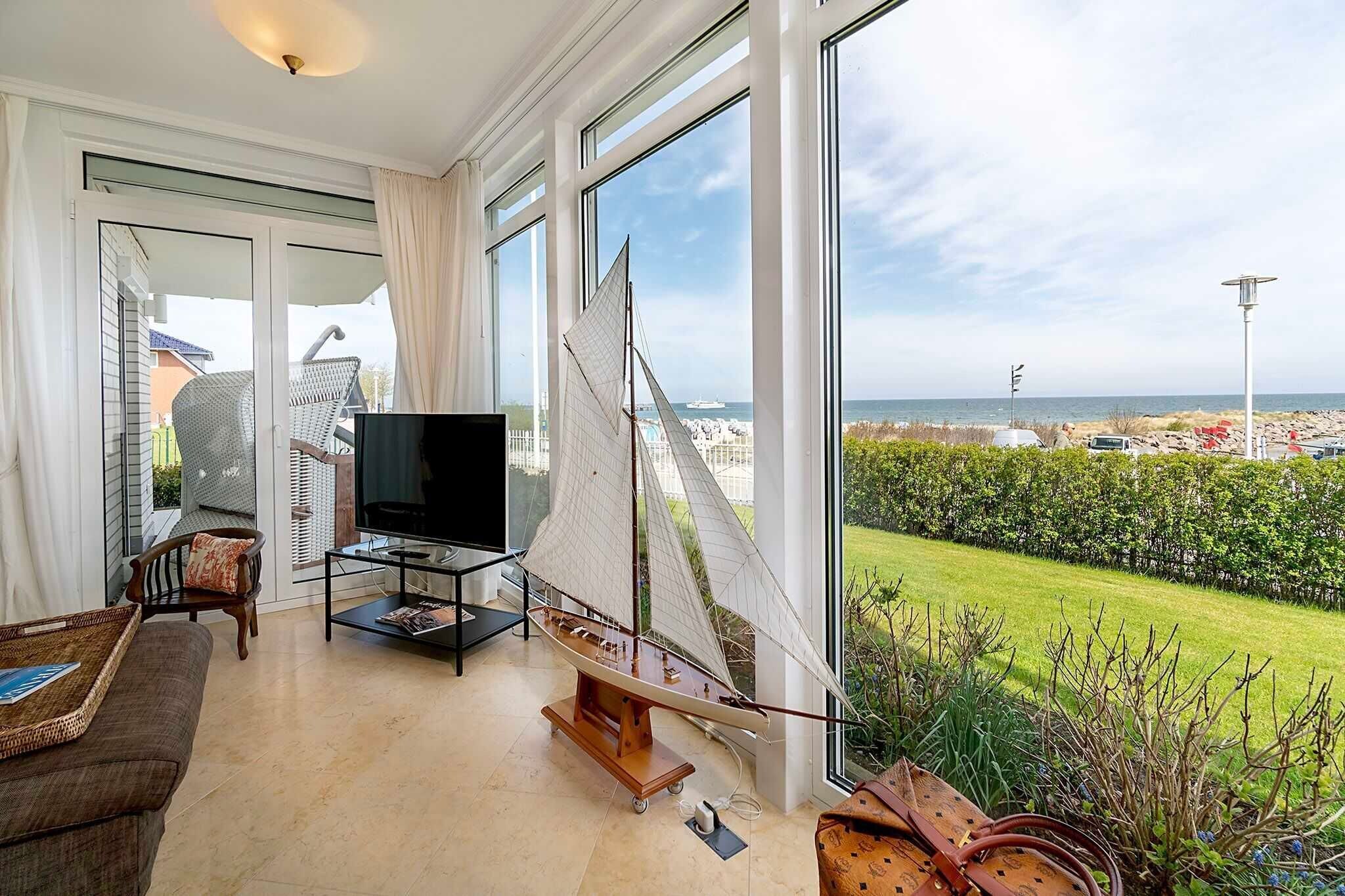 Un salon moderne avec une maquette de voilier, un téléviseur et une vue sur la mer grâce à de grandes fenêtres.