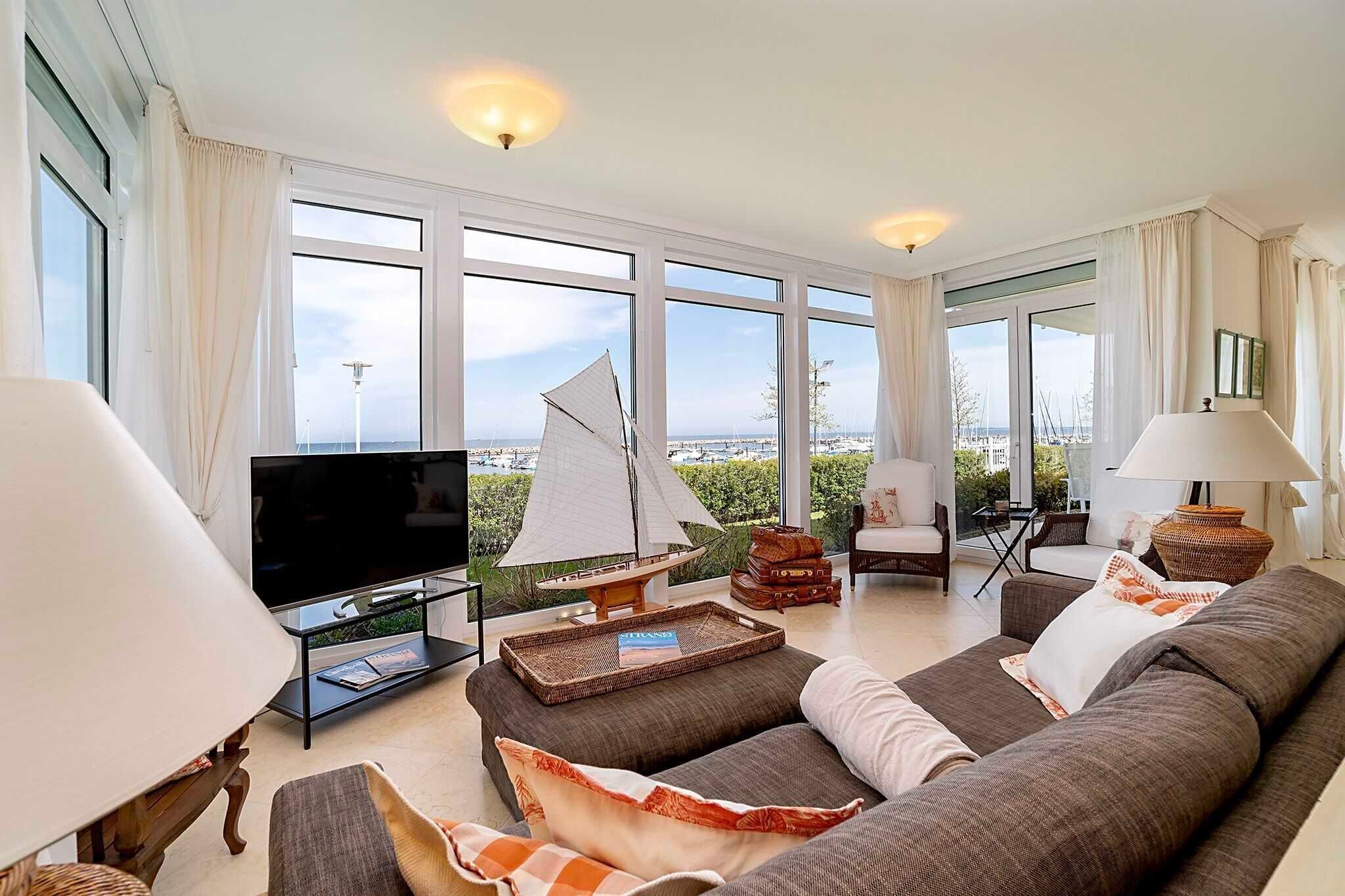A living room with a large window, a television, a sofa, a lamp, and a small sailboat model.
