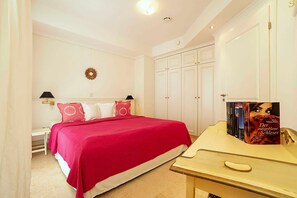 Ein Schlafzimmer mit einem Bett, Nachttischen, einem Kleiderschrank und einem Schminktisch mit Büchern.
