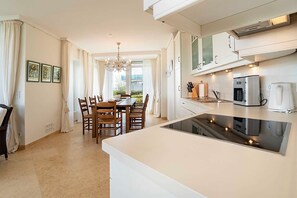 Uma cozinha moderna com fogão embutido, área de jantar com mesa e cadeiras, e vista para o exterior.