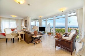 Ein geräumiges Wohnzimmer mit großem Fernseher, bequemen Sitzgelegenheiten und Meerblick.