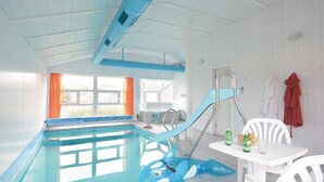 Una piscina con un tobogán azul, una mesa con bebidas y una silla.