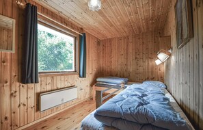 A wooden cabin room with a bed, a window with curtains, a bedside lamp, and a radiator. - Cozy home in Rømø with WiFi (Rømø)