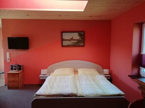 Un dormitorio con una cama, televisor, un cuadro y una mesita con altavoces.