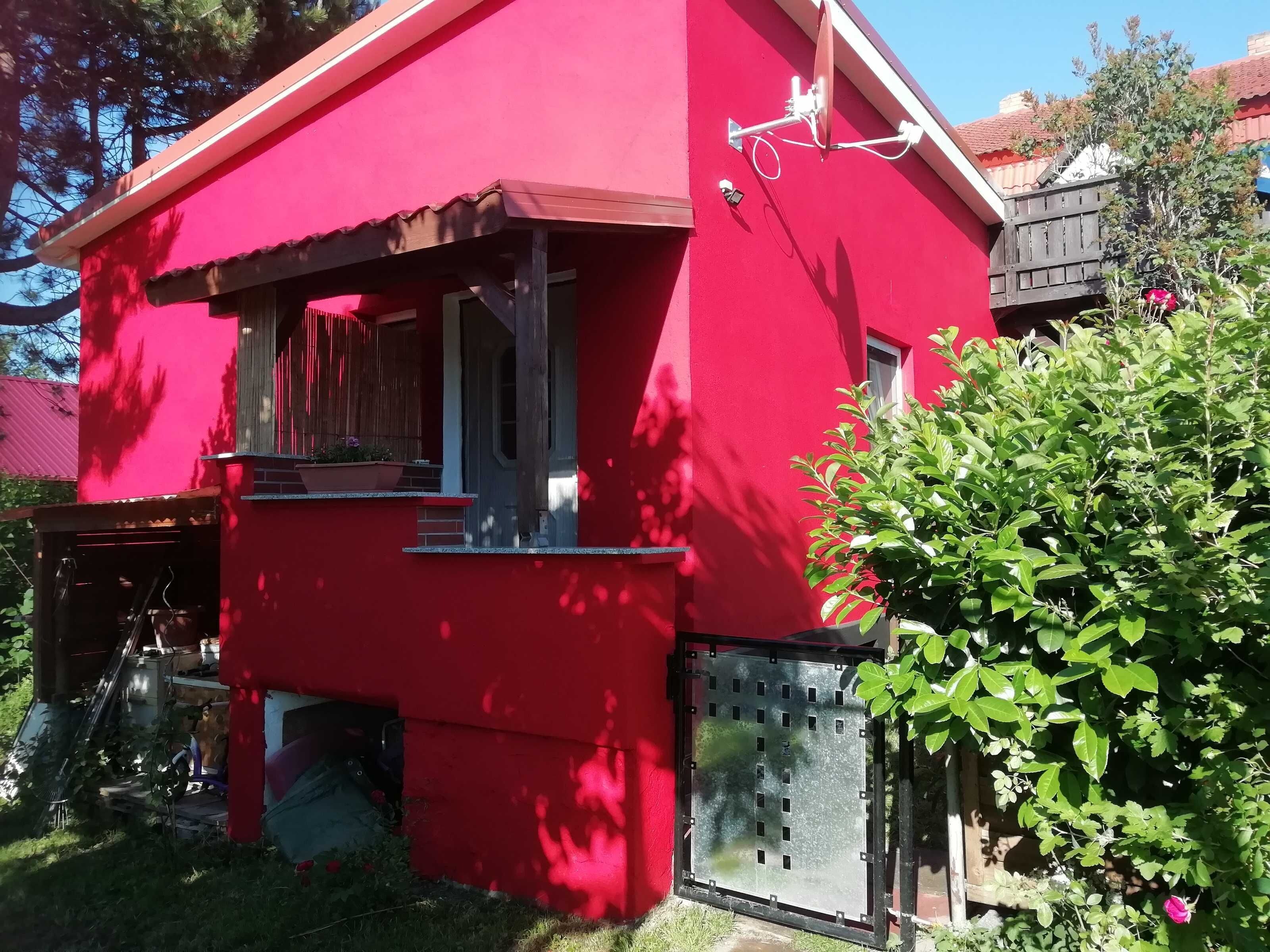 A red building with a small window, a satellite dish, and a metal gate.