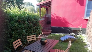 A patio with a table and chairs, a potted plant, and a red building in the background.
