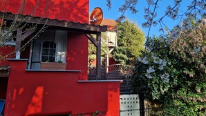 Un bâtiment rouge avec une antenne parabolique, une fenêtre ornée d’un pot de fleurs et un arbre aux fleurs blanches.
