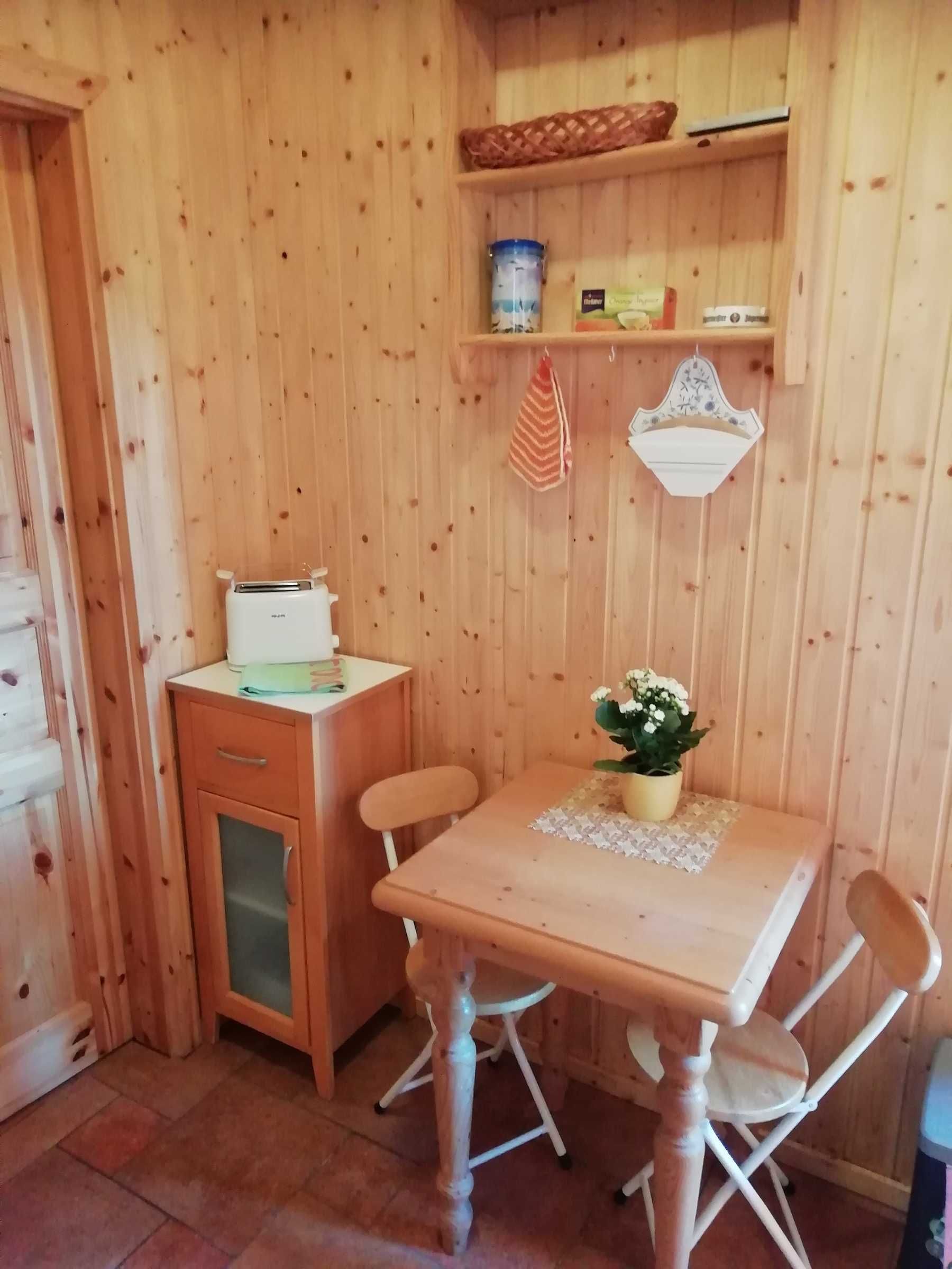 Un interior de madera con una kitchenette, una mesa de comedor con sillas y un estante con utensilios de cocina.