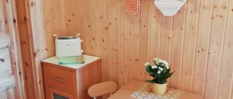 Un interior de madera con una kitchenette, una mesa de comedor con sillas y un estante con utensilios de cocina.