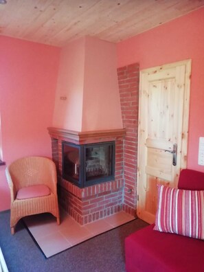 Ein Zimmer mit Kamin aus Backstein, einem Korbsessel, einem roten Sofa und einer Holztür.