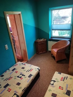 A room with two beds, a window with a view, a chair, and a radiator.