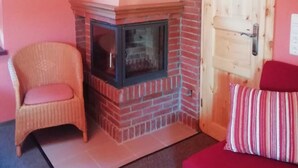 Une pièce avec une cheminée en briques, un fauteuil en osier, un canapé rouge et une porte en bois.