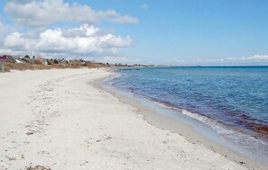 A sandy beach with clear blue water and a few buildings in the background.