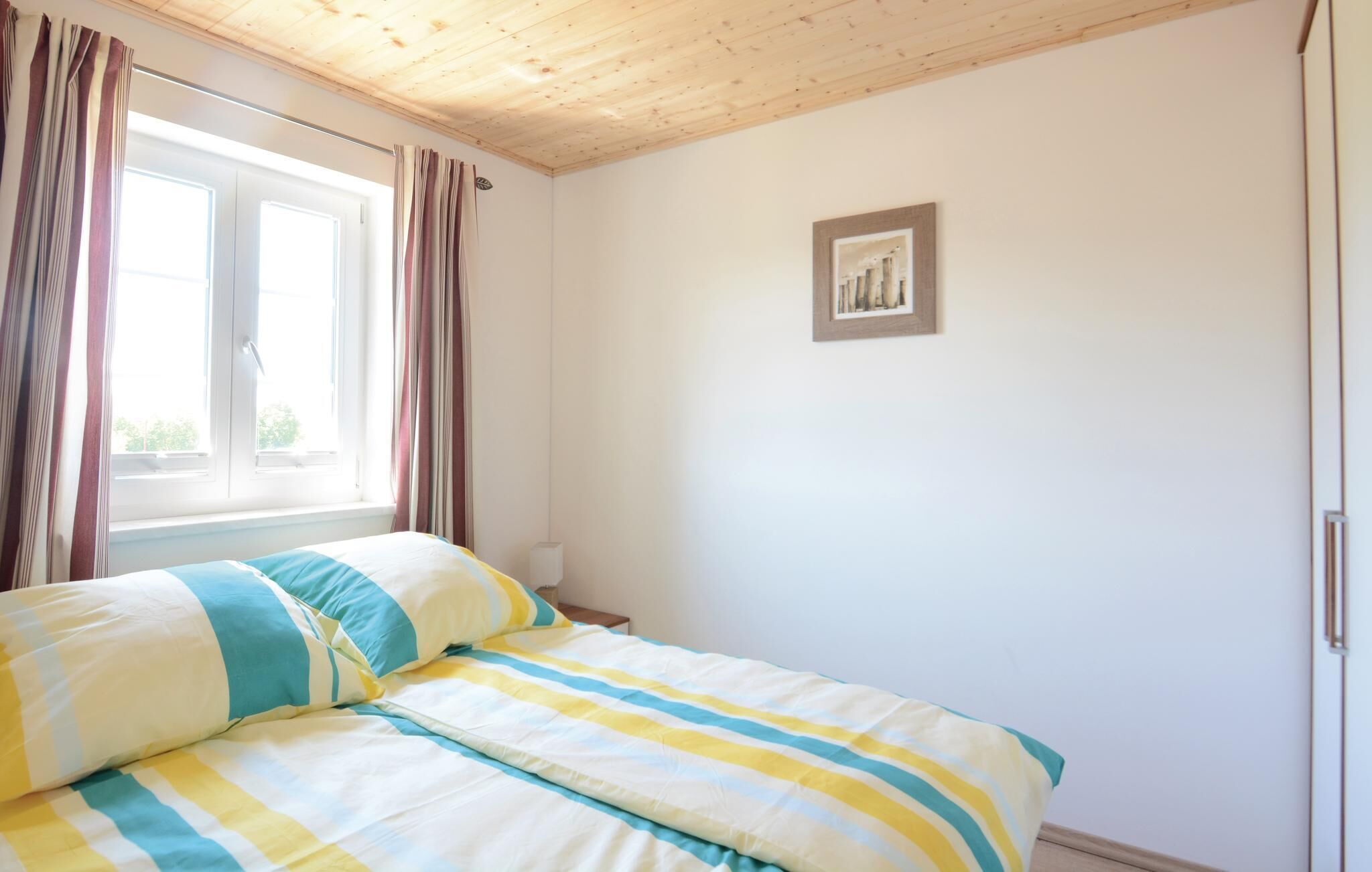 Un dormitorio con cama, cortinas, una ventana y un cuadro en la pared.