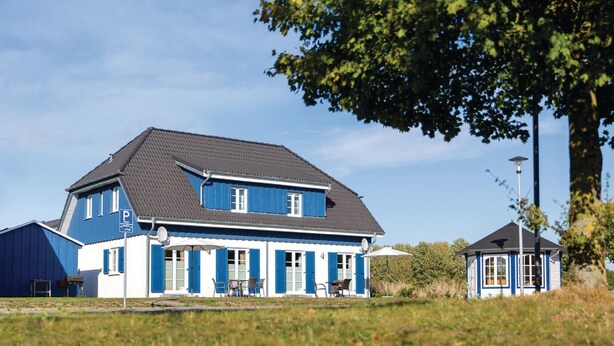 A two-story house with a dark roof and blue exterior walls, featuring a patio with outdoor furniture. - Ferienhaus 6 Altefähr (Altefähr/Rügen)