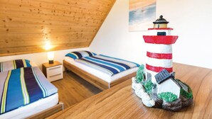 A bedroom with a sloped ceiling, a bed with striped bedding, a nightstand with a lamp, and a decorative lighthouse model. - Ferienhaus 6 Altefähr (Altefähr/Rügen)