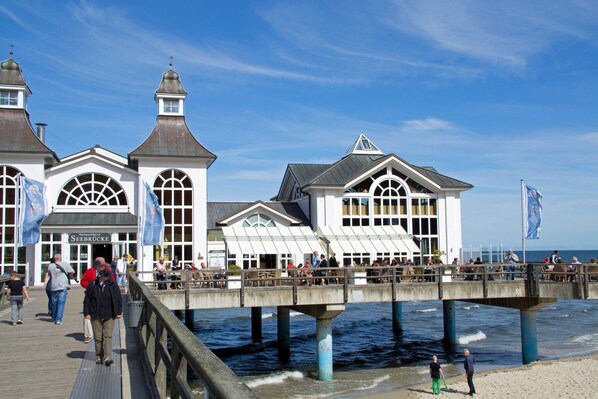 A pier with a white building featuring arched windows and a steep roof, extending over water.