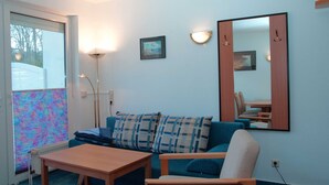 A room with a blue sofa, a wooden table, a floor lamp, and a mirror on the wall. - Sun view with sun terrace 5 min to the Baltic Sea and beach (Sellin)
