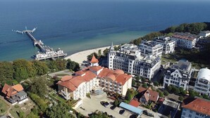 An aerial view of a coastal area with a pier extending into the sea, surrounded by residential buildings with red-tiled roofs and a central building with a dome. - Sun view with sun terrace 5 min to the Baltic Sea and beach (Sellin)