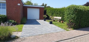 A brick building with a white garage door, a paved driveway, a bench, and a well-maintained hedge. - North Sea House Dornumersiel - house (Dornum)