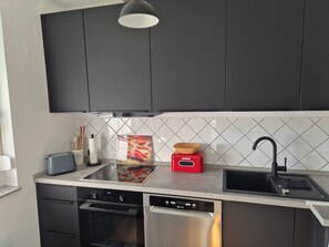 A modern kitchen with dark cabinets, a stainless steel dishwasher, a red toaster, and a black sink. - North Sea House Dornumersiel - house (Dornum)