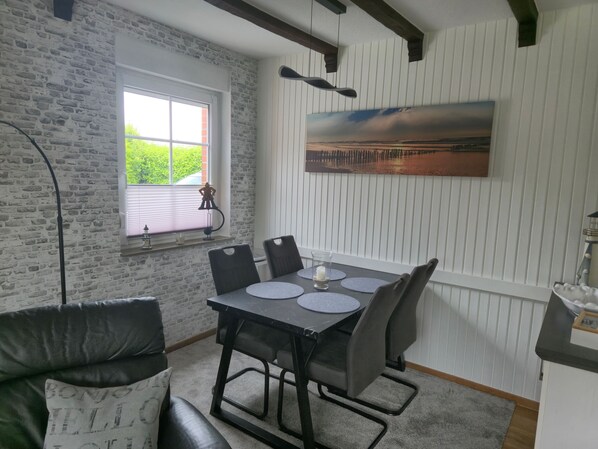 A dining area with a table, chairs, a window, and a painting on the wall.