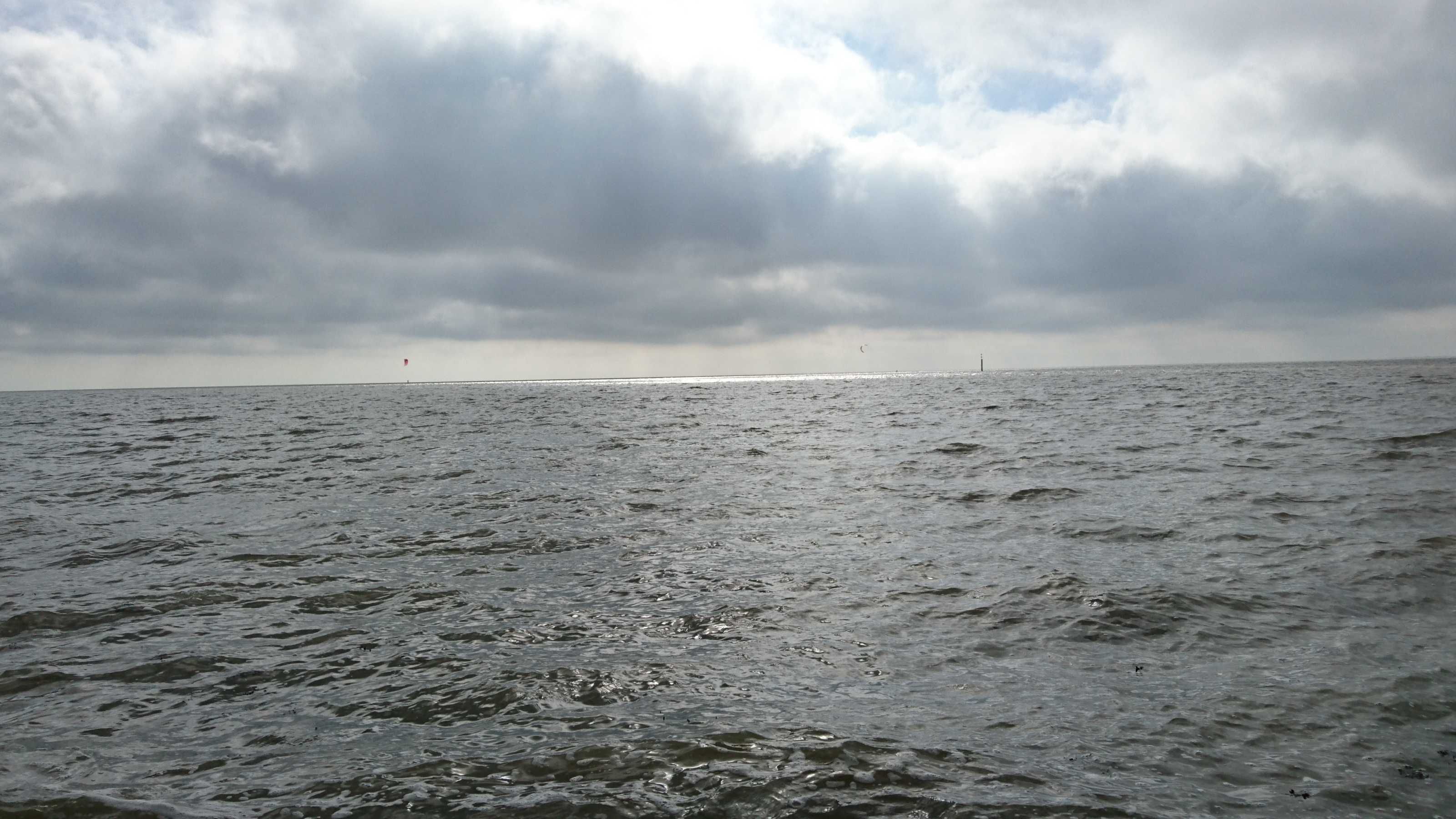 Een wateroppervlak met golven en een bewolkte lucht.