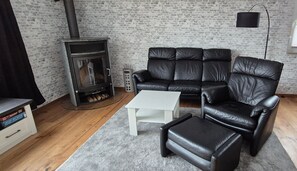 Un salon avec un canapé en cuir noir, une table basse blanche, une cheminée et un mur en briques.