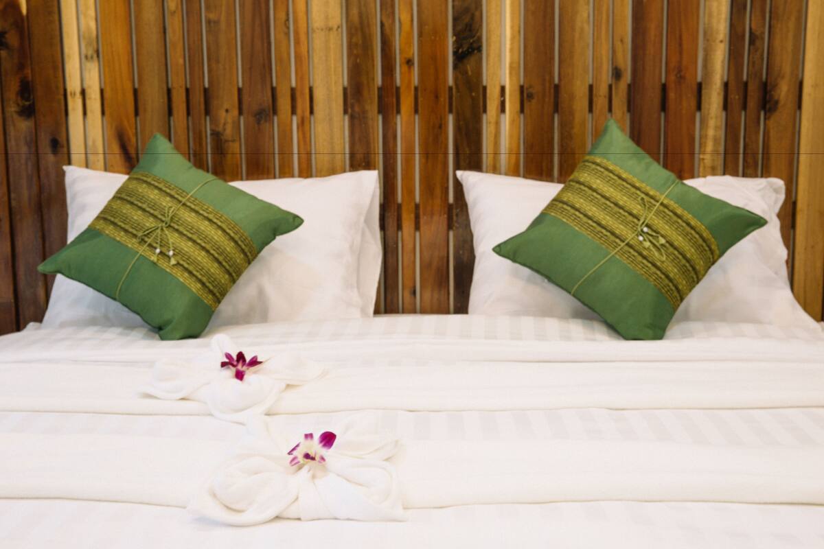 Una cama bien hecha con sábanas blancas y dos almohadas verdes con adornos dorados.