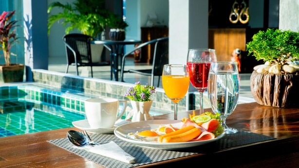 A dining table with a plate of food, a glass of orange juice, and a glass of water by a poolside. - Baan Chankaew Hotel (Ko Pha-ngan)