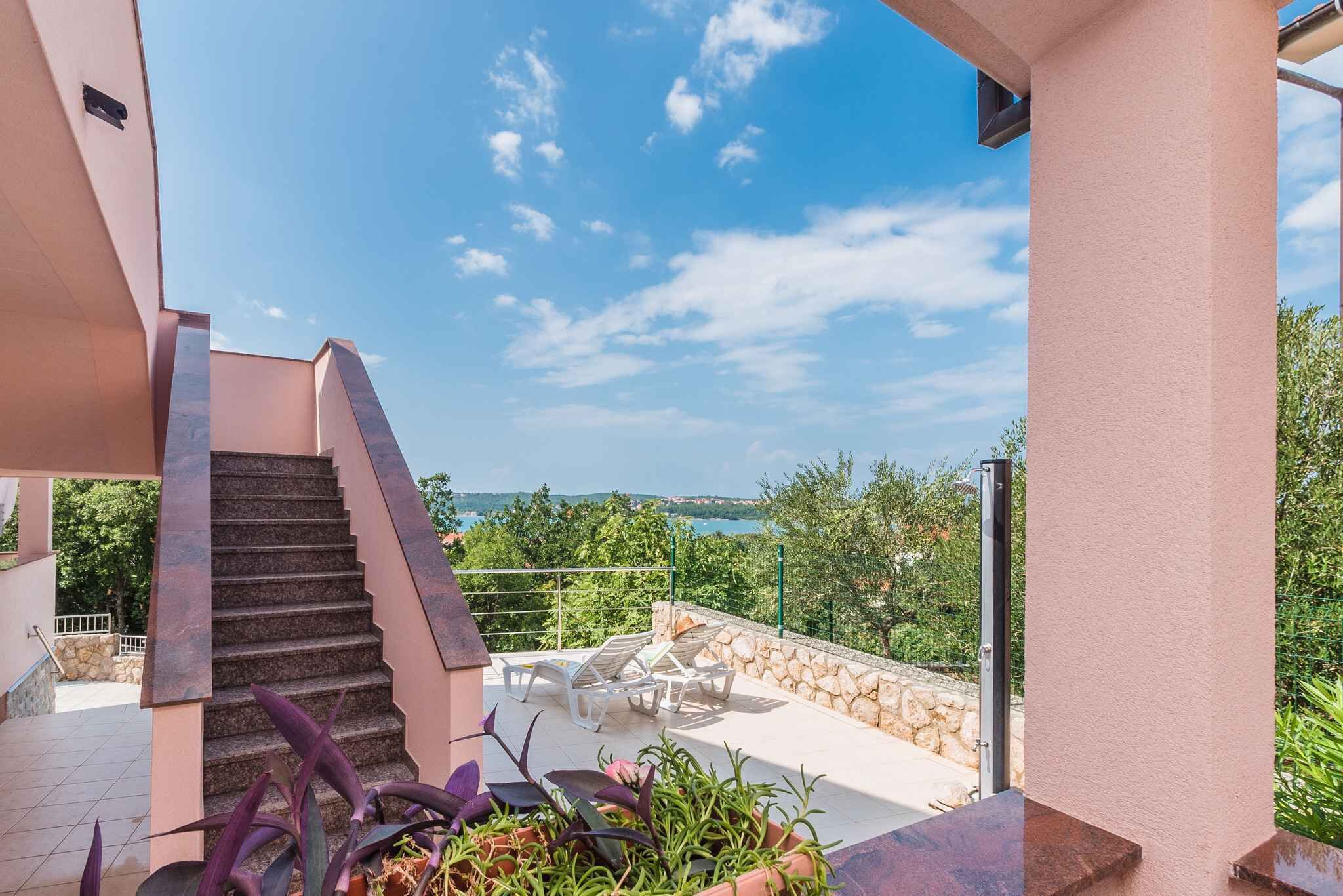 Eine Treppe führt zu einer Terrasse mit Gartenmöbeln und Blick auf das Meer.