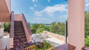Eine Treppe führt zu einer Terrasse mit Gartenmöbeln und Blick auf das Meer.