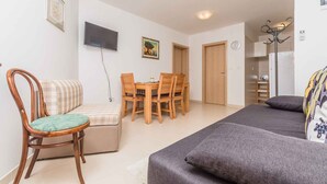 Ein Wohnzimmer mit einer Couch, einem Esstisch mit Stühlen, einem an der Wand montierten Fernseher und einem Kühlschrank.