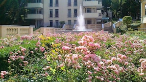 Ein Gebäude mit mehreren Balkonen, einer Fontäne und einem Garten mit rosa Blüten.
