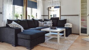 Una sala moderna con un sofá seccional gris oscuro, una mesa de centro blanca y un aparador de vidrio con objetos decorativos.