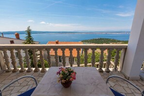 Ein Balkon mit Tisch und Stühlen mit Blick auf die Küste, einschließlich Gebäude und Grünflächen.