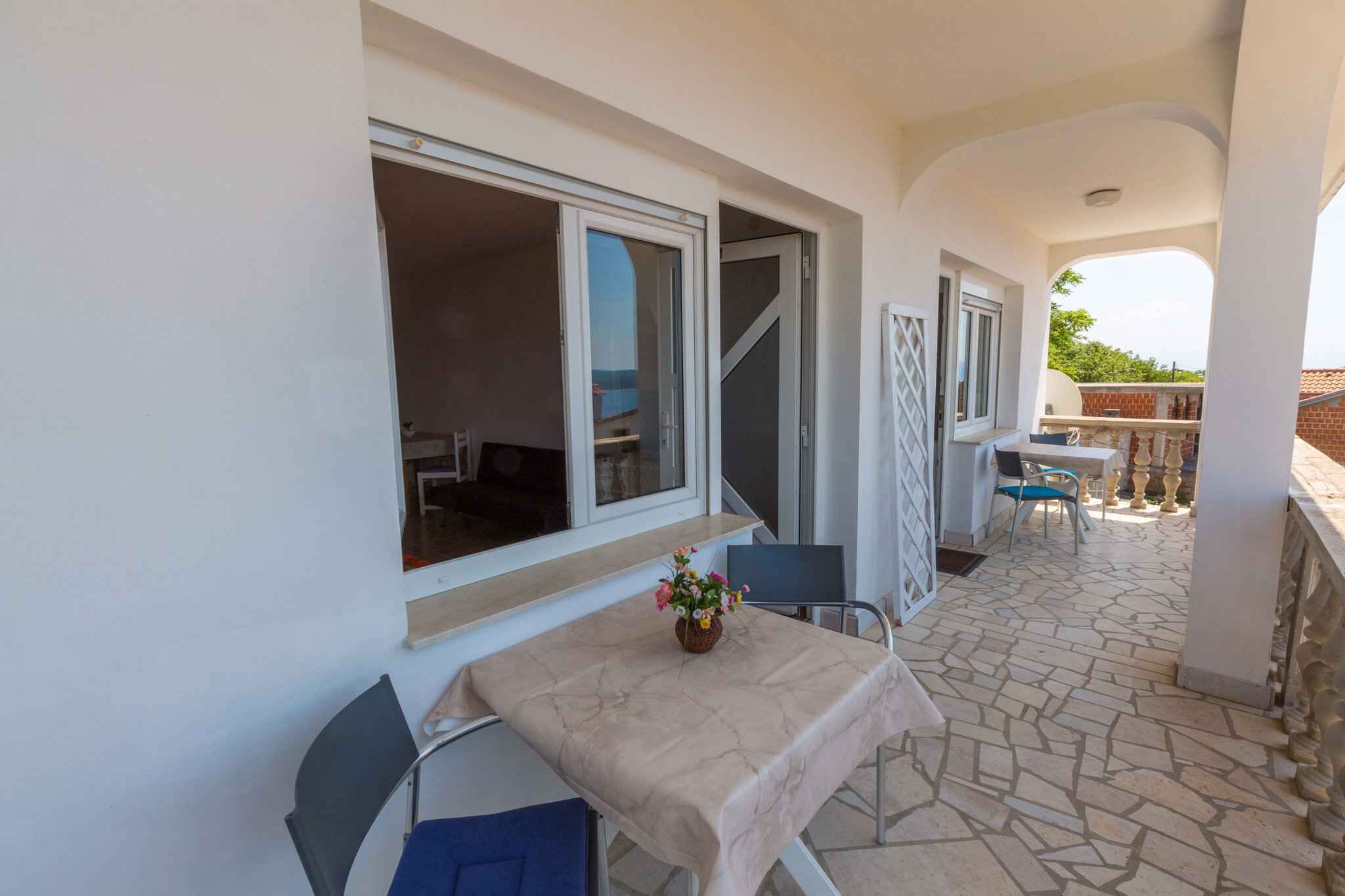 A balcony with a table and chairs, a window, and a view of the surrounding area.