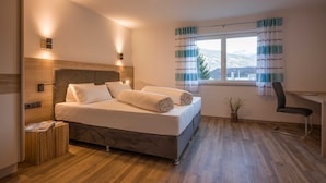 Un dormitorio moderno con cama, lámparas de noche, un escritorio y vistas a las montañas desde la ventana.
