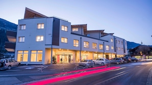 Un hotel de varios pisos con diseño moderno, que cuenta con una entrada destacada, un área de estacionamiento y vistas del paisaje circundante.