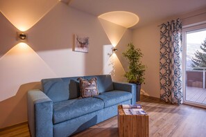 Un sofá azul con un cojín, una mesa de centro de madera, una planta en maceta y un aplique de pared.