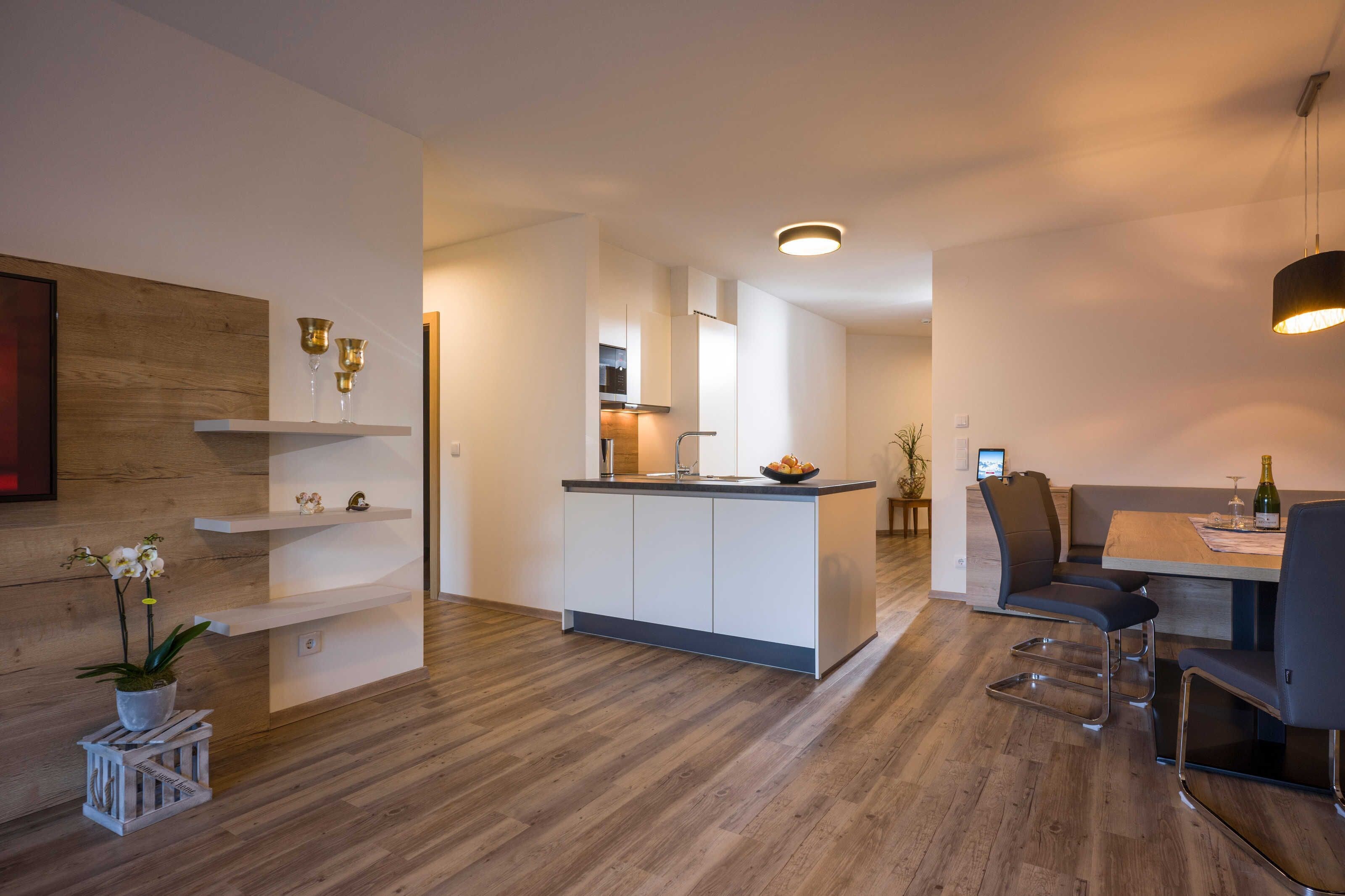 A modern kitchen with a central island, white cabinetry, and a dining area with a table and chairs.