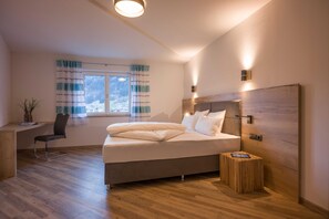 A modern bedroom with a bed, a desk, a chair, a window with curtains, and a wooden headboard. - Apartment Mountain Deluxe - Aparthotel **** AlpTirol (Kaltenbach)
